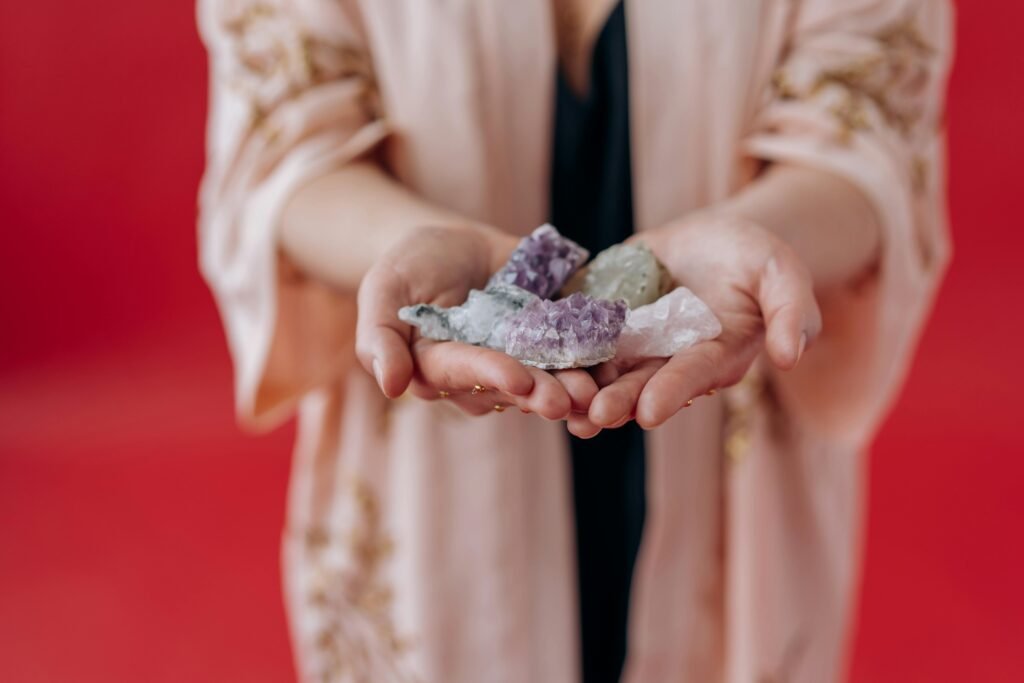 pexels photo 6932006 6932006 Elegant hands holding healing crystals against a vibrant red background.