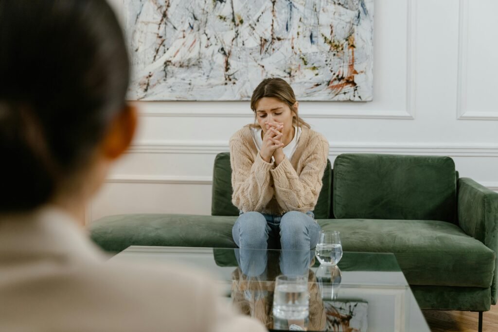 Woman in therapy session, seated on a green couch indoors, looking pensive.
